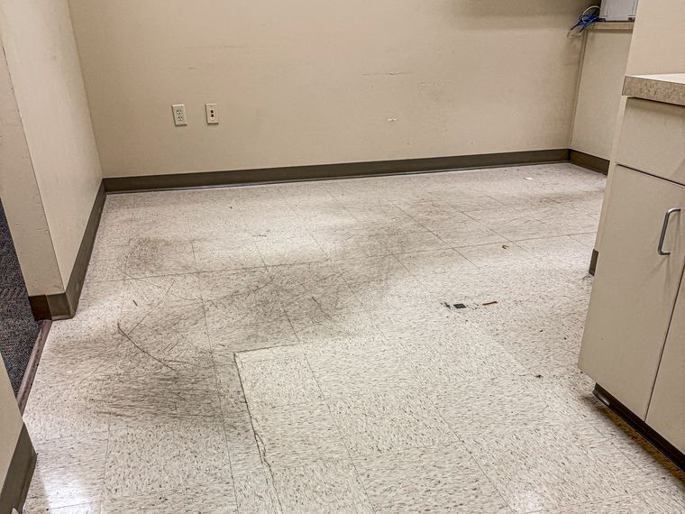 Copy room tile floor before stripping, with heavy scuff marks and a dulled finish