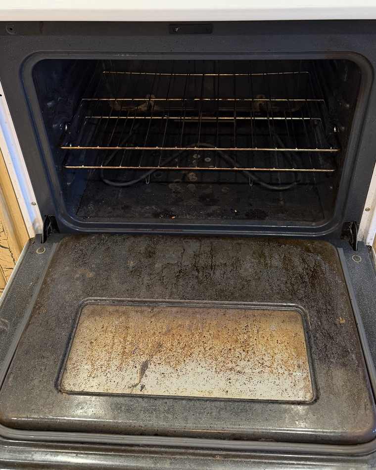 Oven interior before cleaning, with baked-on grease across the door, racks and oven floor
